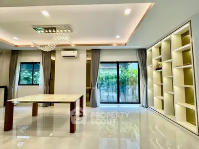 Spacious modern living room with elegant chandelier and large windows overlooking greenery.