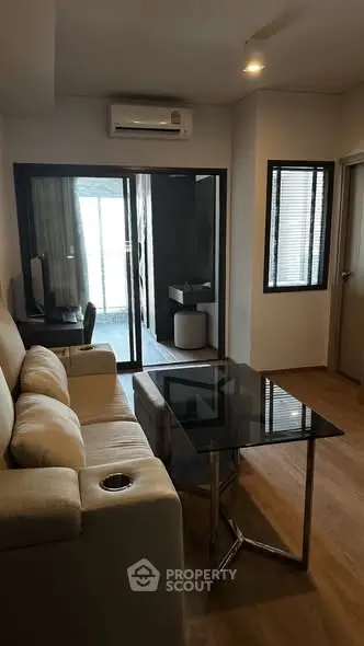 Modern living room with glass table and beige sofa, featuring a view into a stylish bathroom.