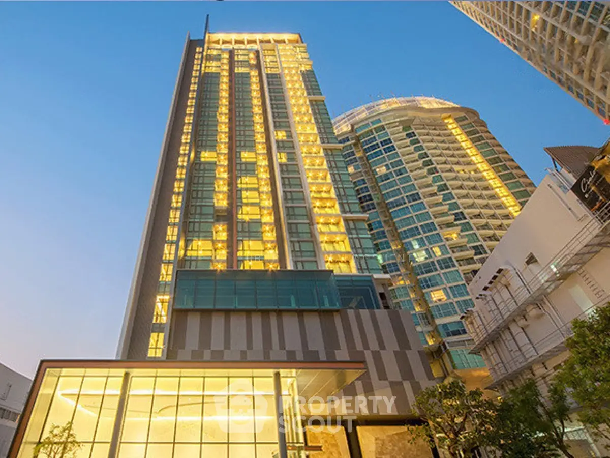 Stunning modern high-rise building with illuminated windows against a clear blue sky, showcasing urban luxury.