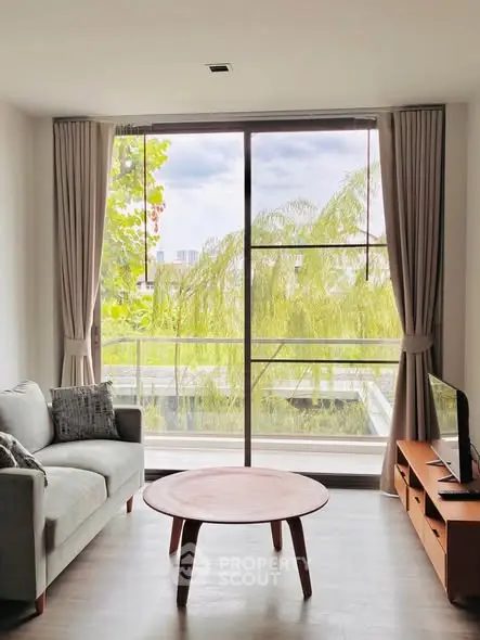 Bright living room with large window and modern furniture, offering a serene view of greenery.