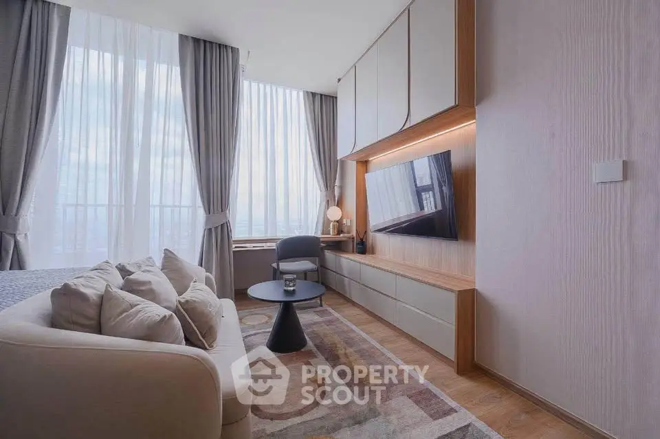 Modern living room with large windows, stylish furniture, and a mounted TV, offering a bright and cozy atmosphere.