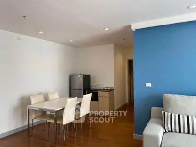 Modern living room with dining area and kitchen featuring sleek furniture and vibrant blue accent wall.