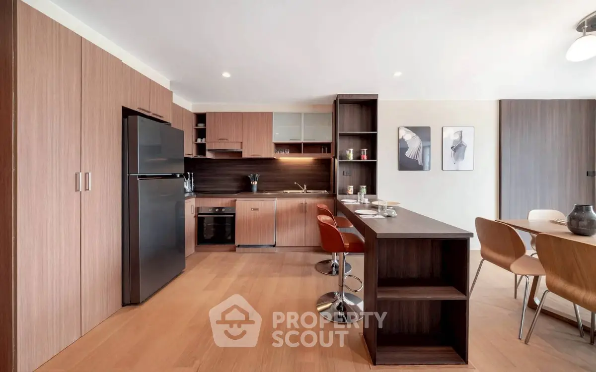 Modern kitchen with sleek wooden cabinetry and dining area in open layout apartment