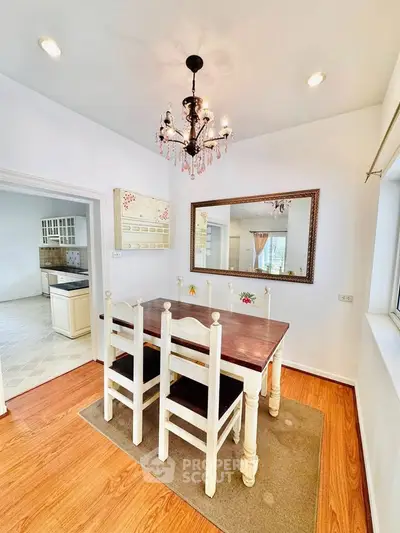 Charming dining area with elegant chandelier and rustic wooden table in bright, airy home.