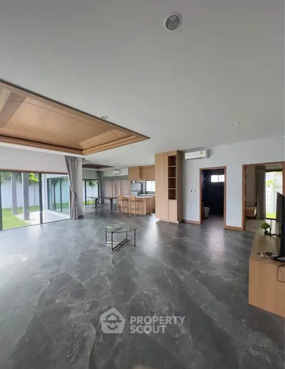 Spacious modern living room with open kitchen and large windows overlooking garden.