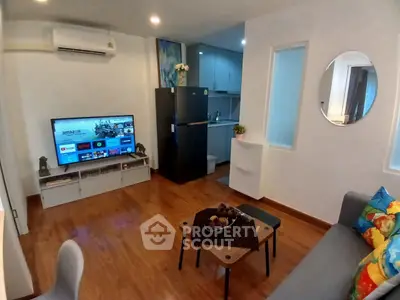 Modern living room with TV, air conditioning, and compact kitchen in cozy apartment.