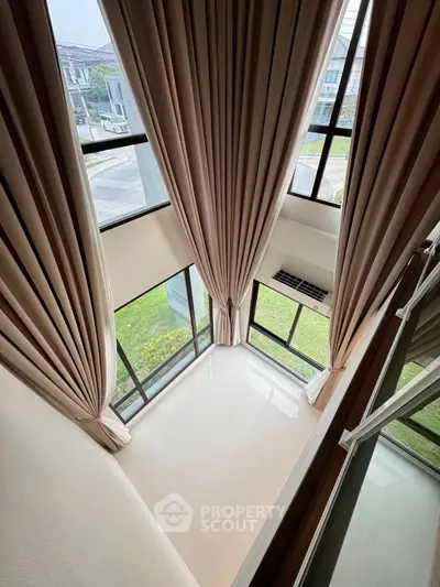 Stunning double-height living room with floor-to-ceiling windows and elegant curtains, offering a bright and airy ambiance.