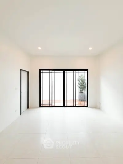 Spacious minimalist room with large window and sleek tile flooring, perfect for modern living.