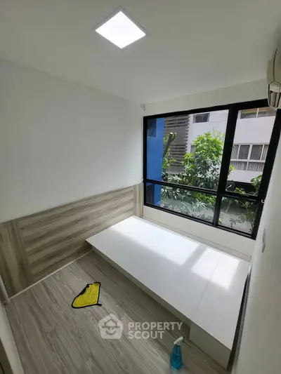 Compact room with large window and wooden flooring, ideal for cozy living space.