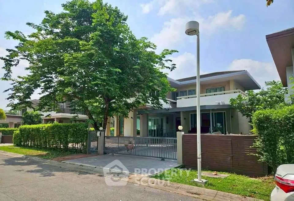 Modern two-story house with lush greenery and gated entrance in a serene neighborhood.