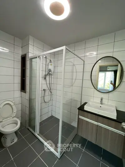 Modern bathroom with glass shower, round mirror, and sleek vanity in contemporary home.