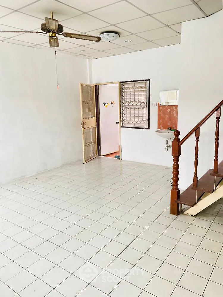 Spacious tiled living room with ceiling fan and staircase, ideal for family gatherings.
