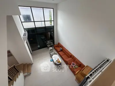 Spacious modern living room with high ceiling and large windows, featuring a stylish orange sofa and elegant decor.