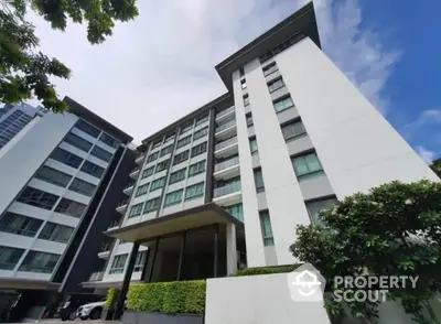 Modern high-rise residential building with lush greenery and clear blue sky.