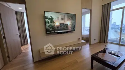 Modern living room with wall-mounted TV and wooden flooring, featuring a glimpse of a cozy bedroom.