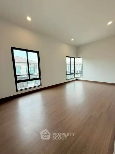 Spacious empty room with large windows and wooden flooring, perfect for customization.