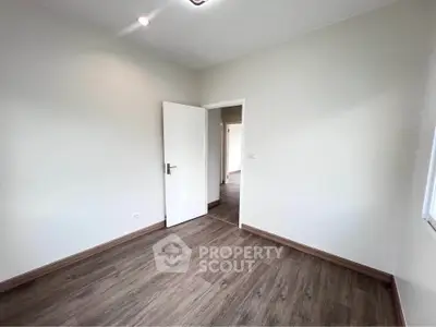 Spacious empty room with wooden flooring and white walls, perfect for customization.