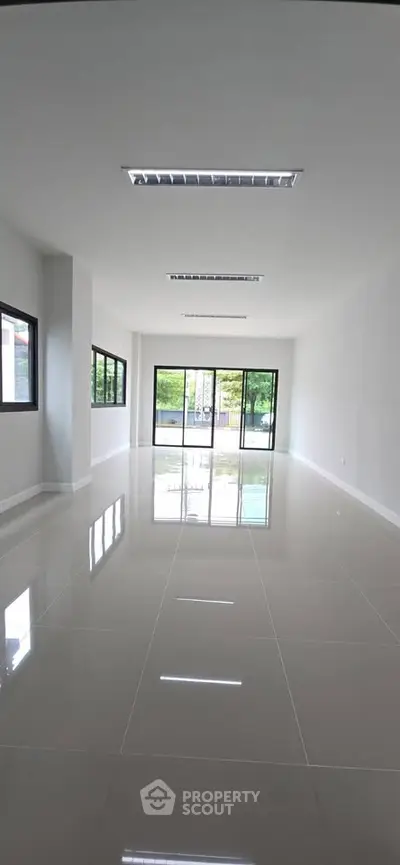 Spacious modern living room with large windows and glossy tiled flooring, offering abundant natural light.
