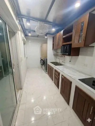 Modern kitchen with sleek cabinetry and appliances in a narrow layout, featuring a washing machine.