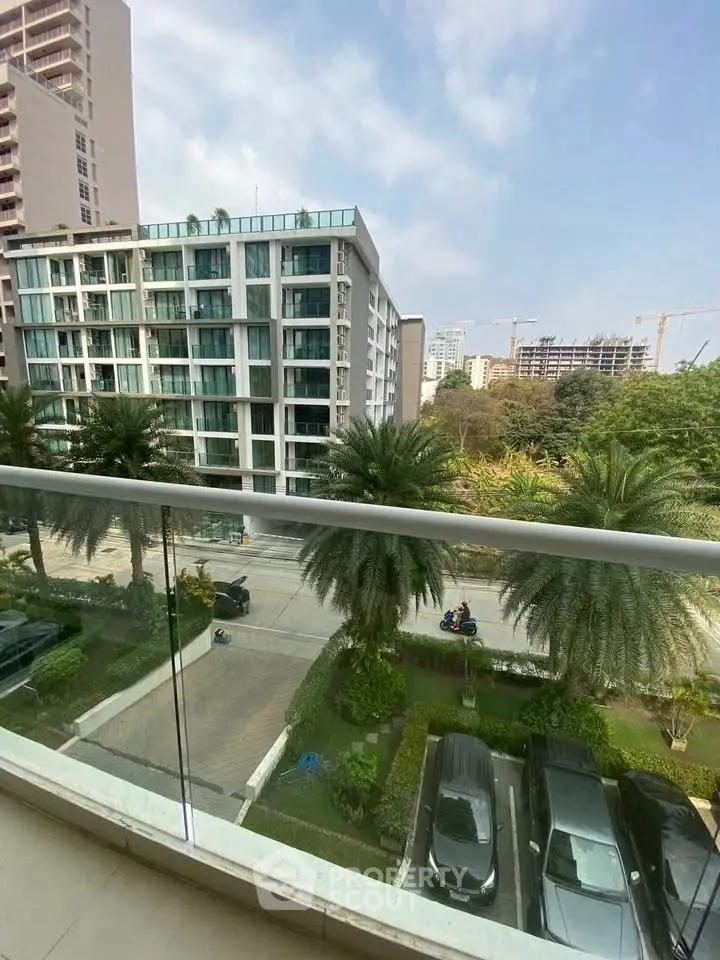 Modern urban apartment view with glass balcony overlooking lush greenery and cityscape.