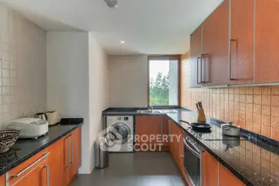 Modern kitchen with sleek wooden cabinets, granite countertops, and built-in appliances including a washing machine.