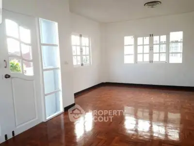 Spacious empty room with polished wooden floors and large windows.