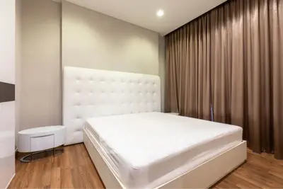 Spacious modern bedroom with elegant design and large bed, featuring floor-to-ceiling curtains and wooden flooring.