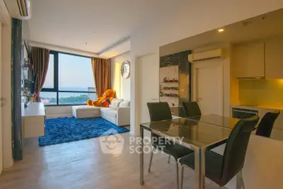 Modern living room with large window and cozy seating area, featuring a plush blue rug and stylish dining space.