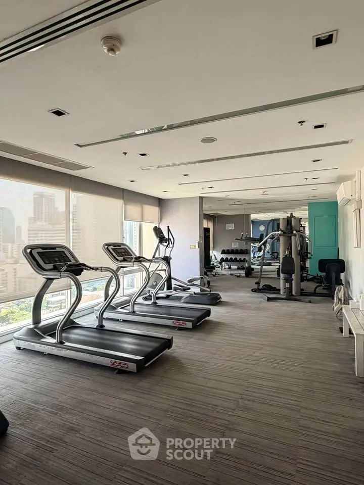 Modern gym with city view, featuring treadmills and fitness equipment in a high-rise building.