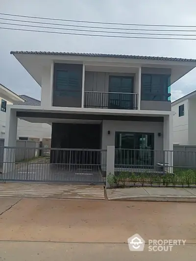 Modern two-story house with balcony and gated driveway in suburban neighborhood.