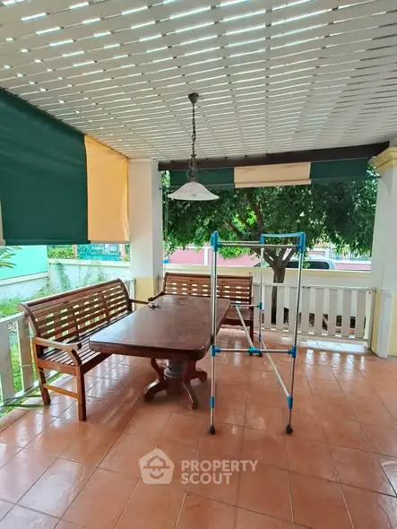 Charming covered patio with wooden furniture and lush garden view, perfect for outdoor relaxation.