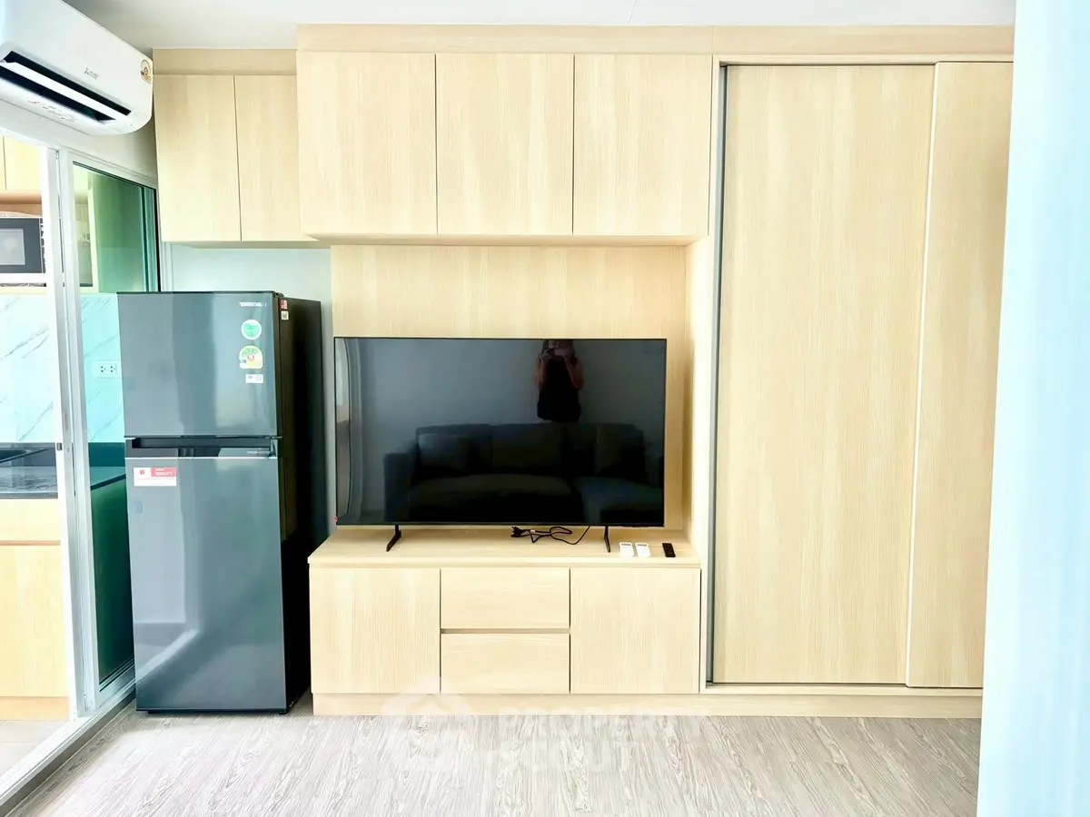 Modern living room with sleek wooden cabinetry and large flat-screen TV, adjacent to a compact kitchen area.