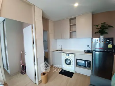 Modern kitchen with washing machine, microwave, and sleek cabinetry in compact apartment.