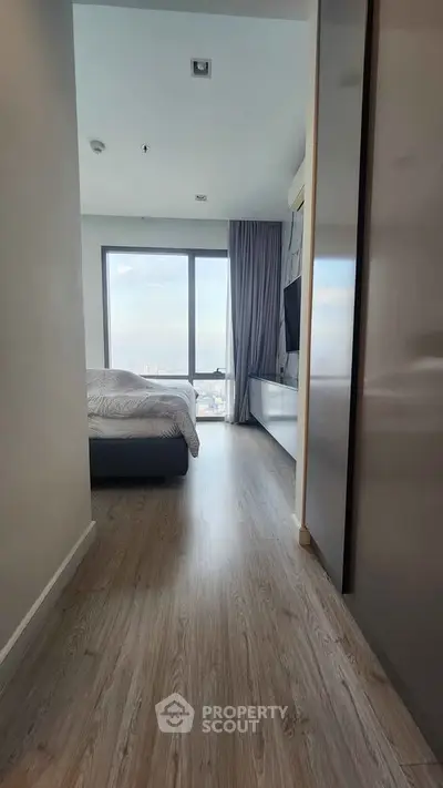 Modern bedroom with large window offering stunning city view, featuring sleek wooden flooring and contemporary decor.