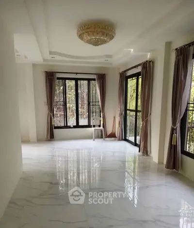 Spacious living room with elegant chandelier and large windows offering natural light and garden views.