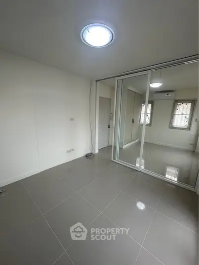 Spacious bedroom with mirrored closet doors and modern tile flooring
