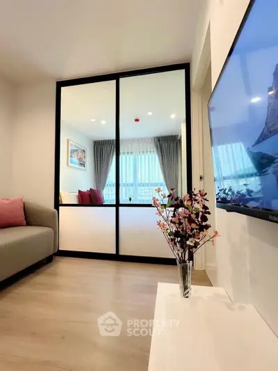 Modern living room with stylish decor and large TV, featuring a cozy seating area and elegant glass partition.