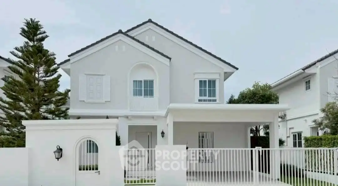 Charming white two-story house with gated entrance and lush greenery.
