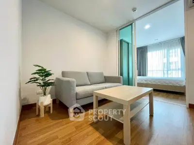 Modern living room with cozy sofa and wooden flooring, adjacent to a bright bedroom with large windows.