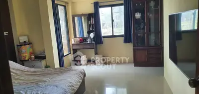 Spacious bedroom with large windows and natural light, featuring a cozy bed and elegant wooden furniture.