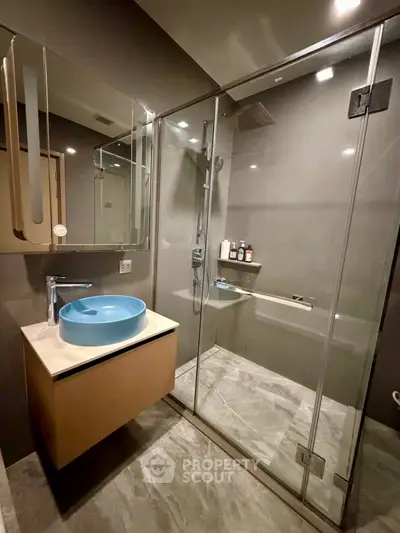 Modern bathroom with glass shower and stylish blue basin in luxury apartment.