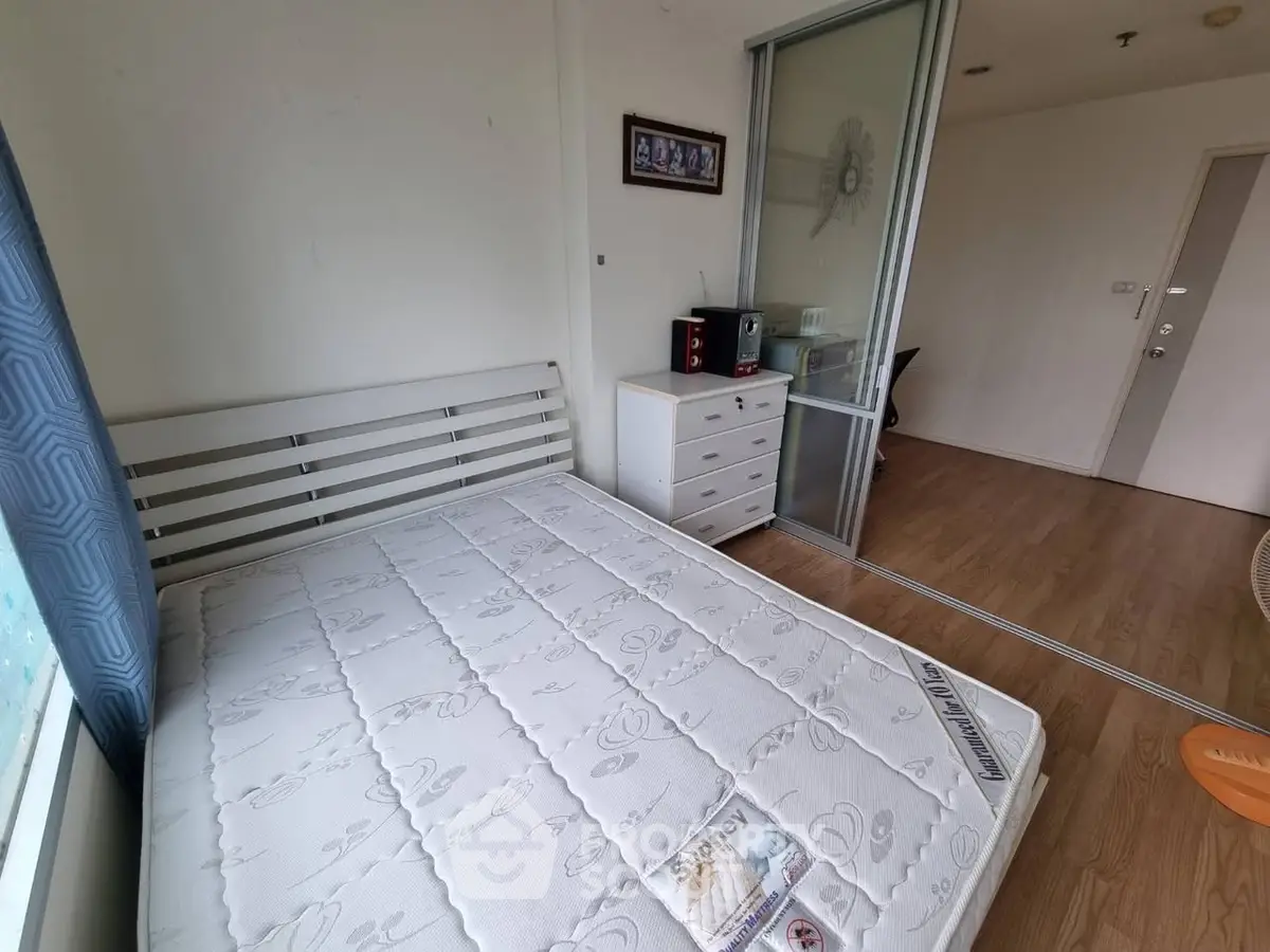 Cozy bedroom with wooden flooring and sliding glass door, featuring a comfortable bed and dresser.