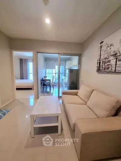 Modern living room with beige sofa and marble coffee table, open layout to dining area and kitchen.