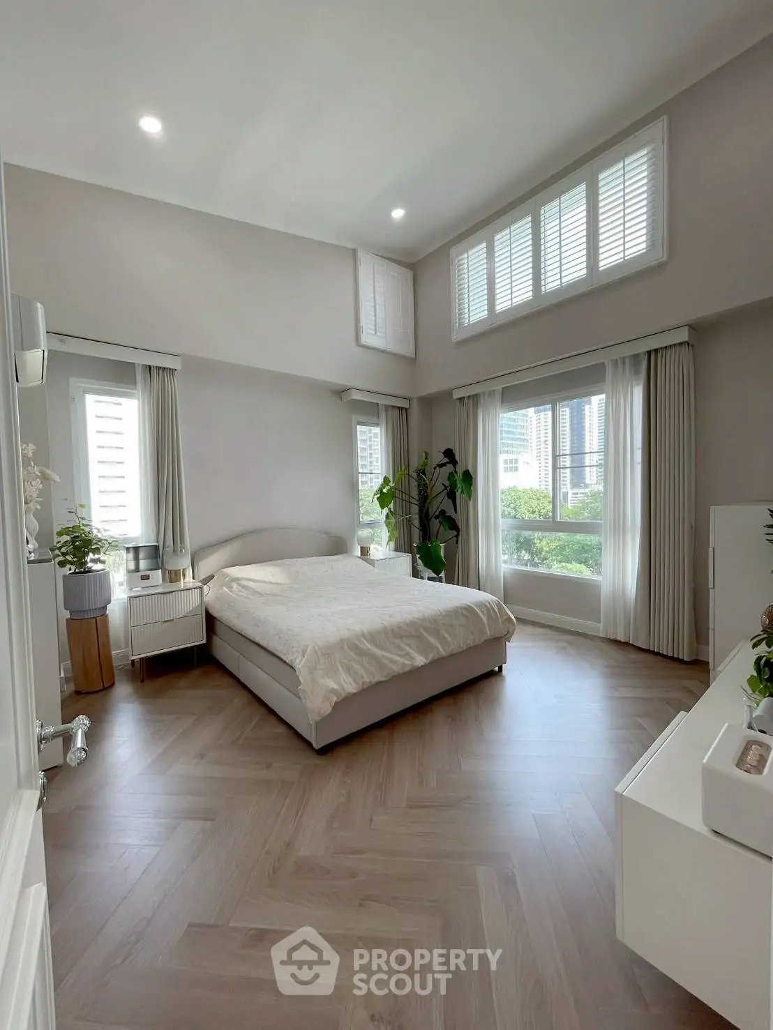 Spacious bedroom with large windows and modern decor, offering a serene and bright atmosphere.