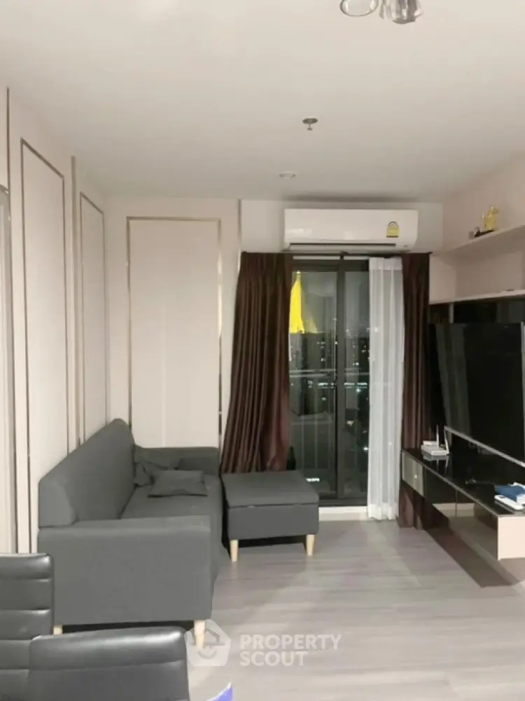 Modern living room with gray sofa and large TV, featuring a balcony view.