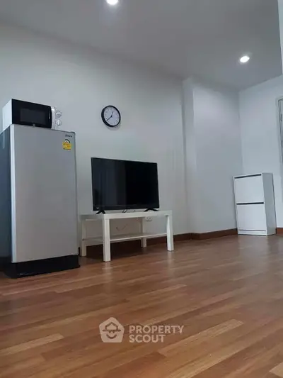 Modern living room with wooden flooring, featuring a sleek refrigerator, TV, and minimalist decor.