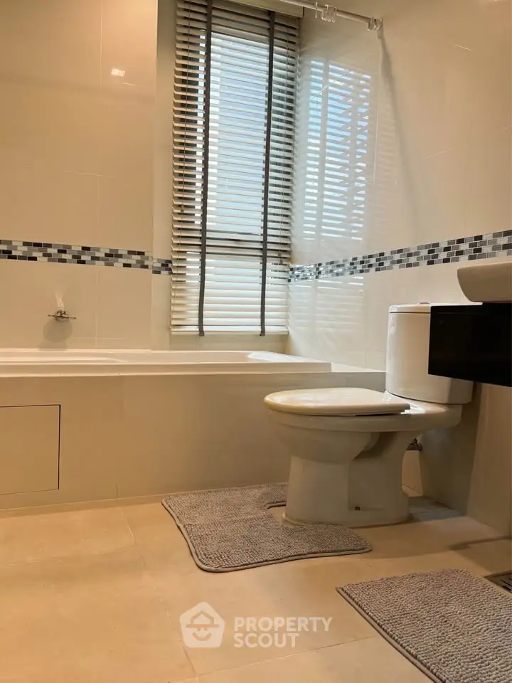 Modern bathroom with bathtub and stylish tiles, featuring natural light through window blinds.