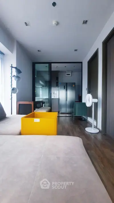 Modern living room with sleek furniture and glass partition leading to kitchen area.