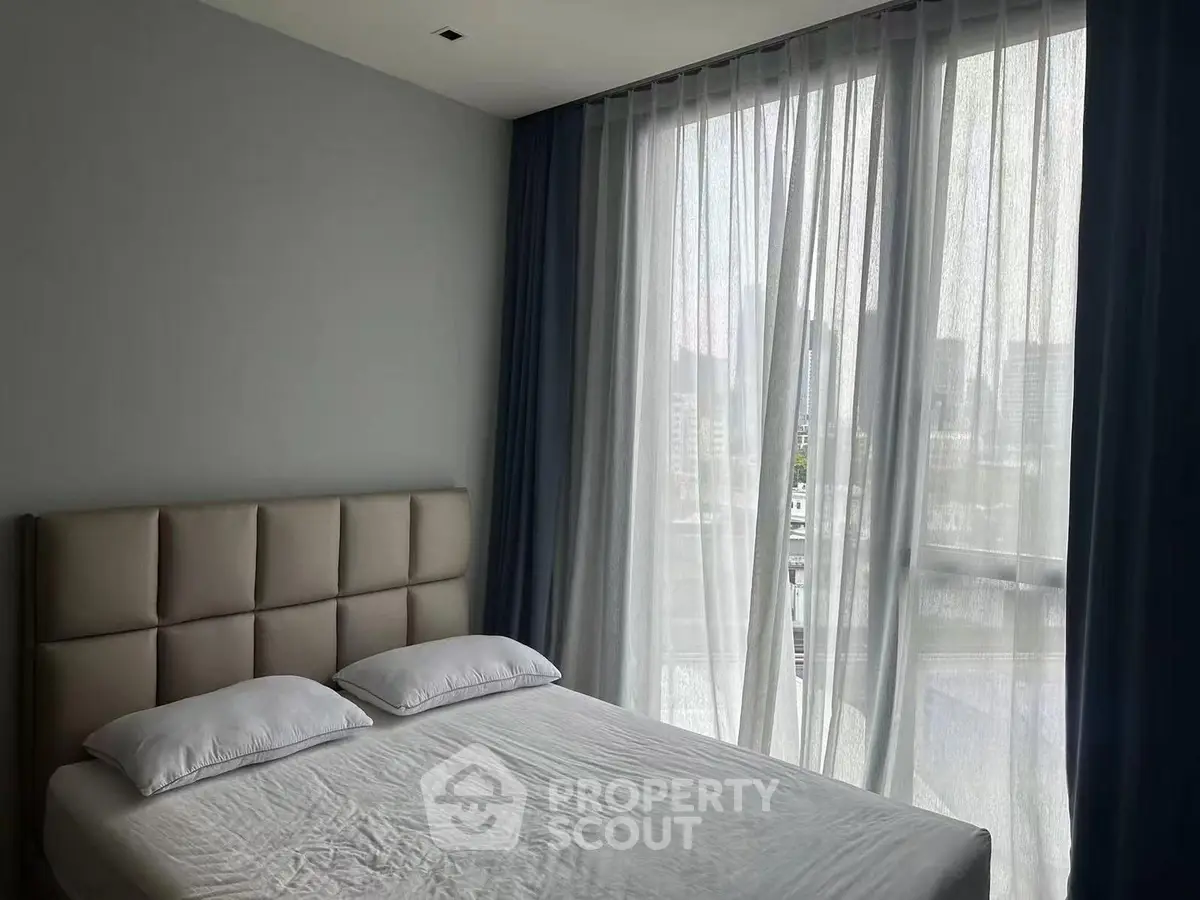 Modern bedroom with large window and city view, featuring a stylish bed and elegant curtains.