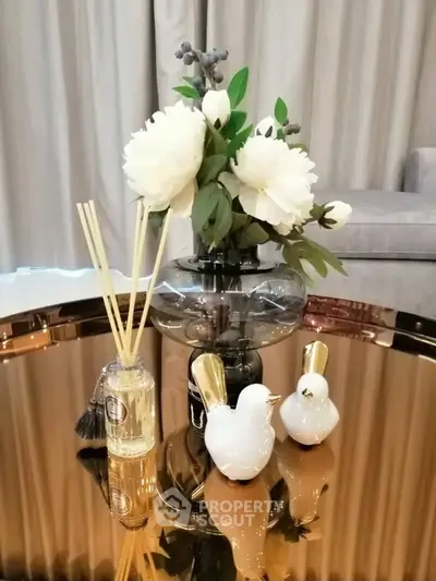 Elegant living room decor with floral arrangement and stylish ornaments on a reflective table.